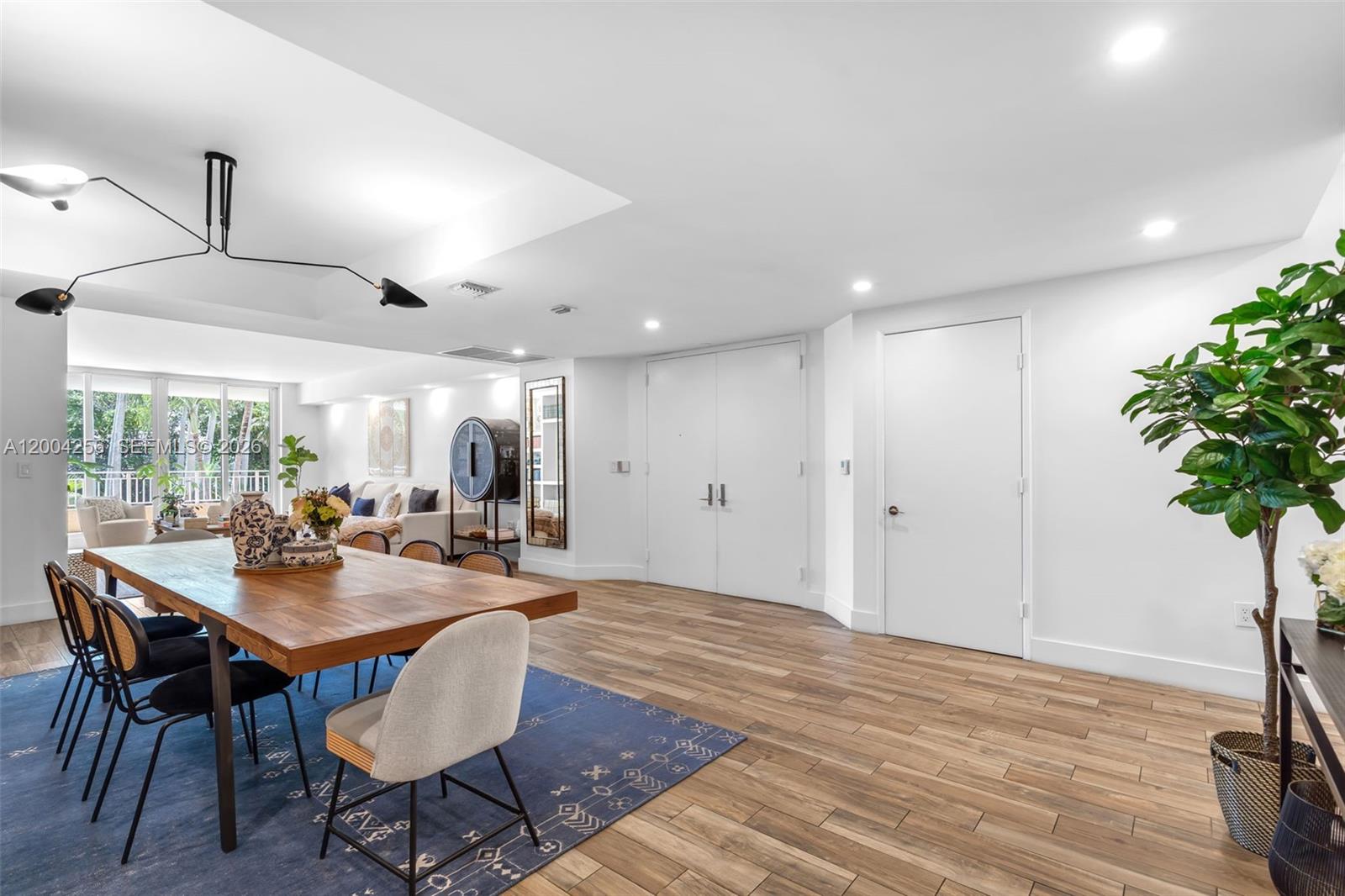 A dining area with a wooden table, blue rug, and white walls leads to a living space — 791 Crandon Blvd # 302, Key Biscayne FL 33149, KEY BISCAYNE, FL