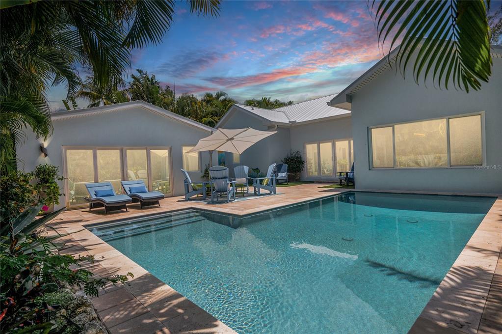 A swimming pool sits on a stone patio in front of a white house — 242 GLADIOLUS STREET, ANNA MARIA, FL