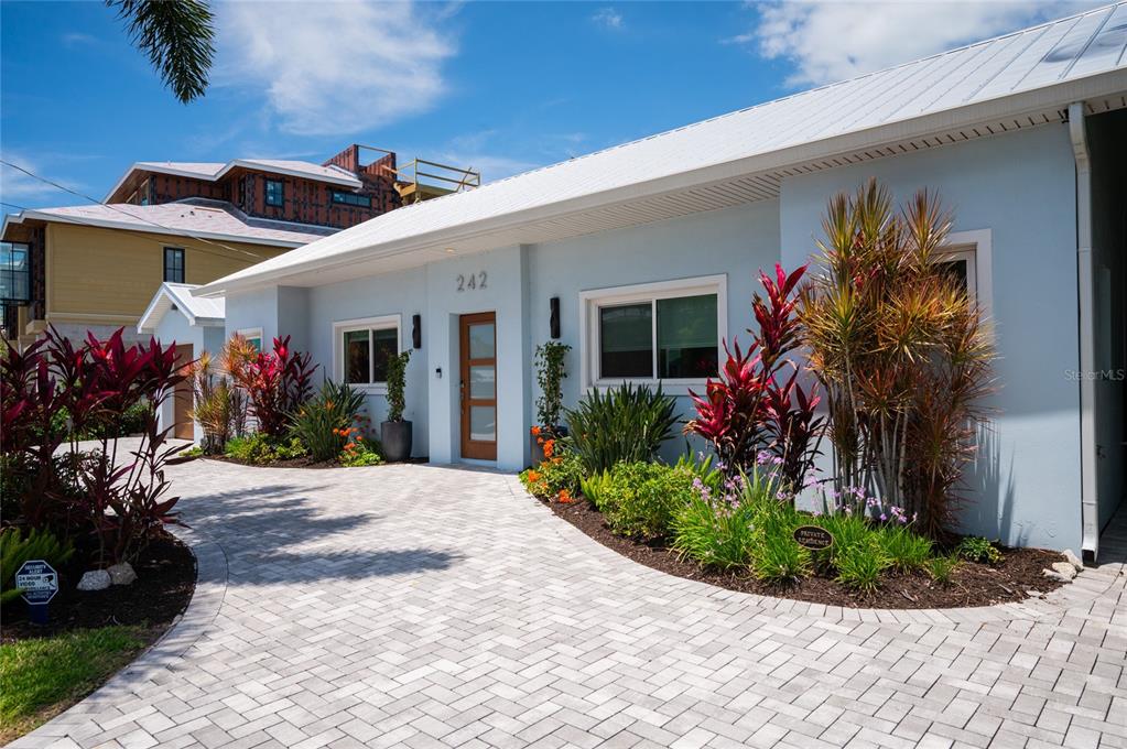 A light blue house with a white roof and a paved driveway features tropical landscaping — 242 GLADIOLUS STREET, ANNA MARIA, FL