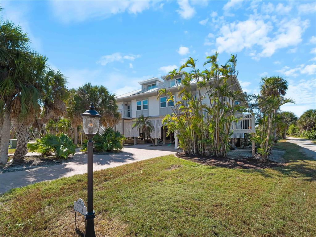 A multi-story house with light siding stands behind a lawn, palm trees, and a lamppost — 7104 PALM ISLAND DRIVE UNIT LE38, PLACIDA, FL