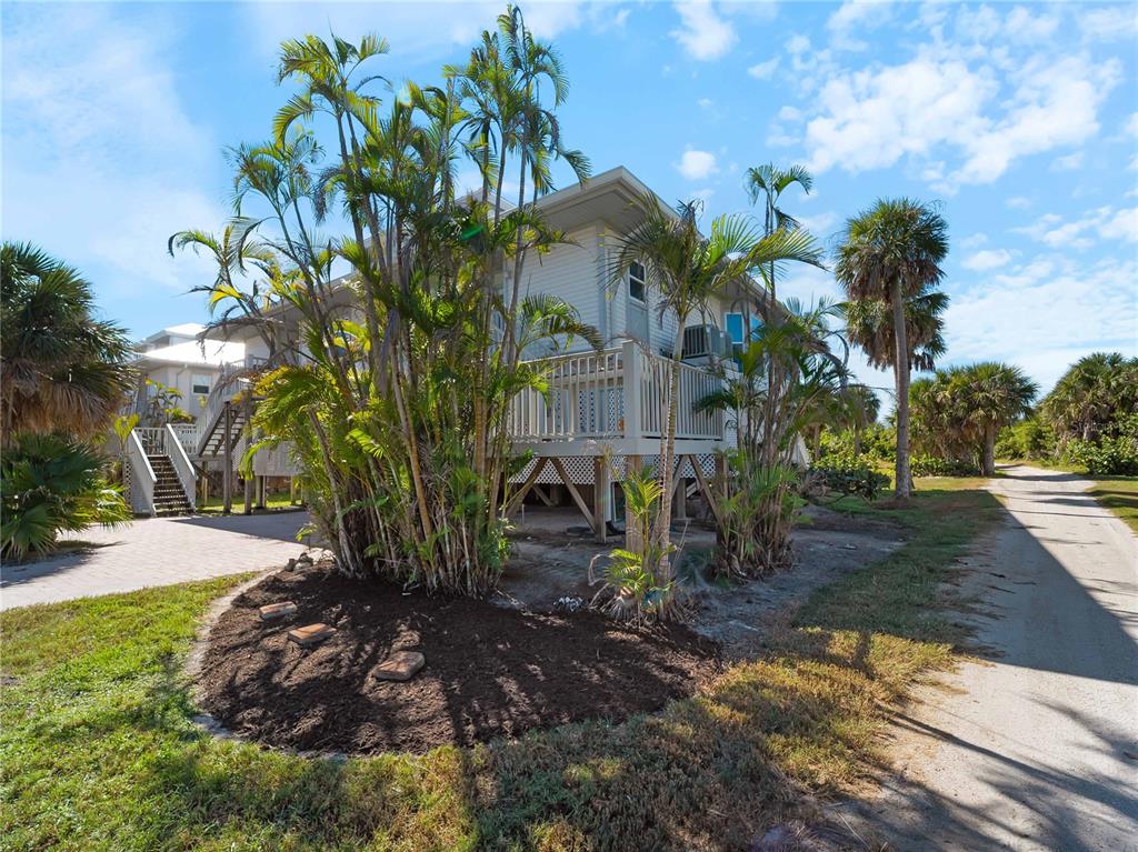 An elevated house with a wooden deck stands behind palm trees next to a dirt road — 7104 PALM ISLAND DRIVE UNIT LE38, PLACIDA, FL