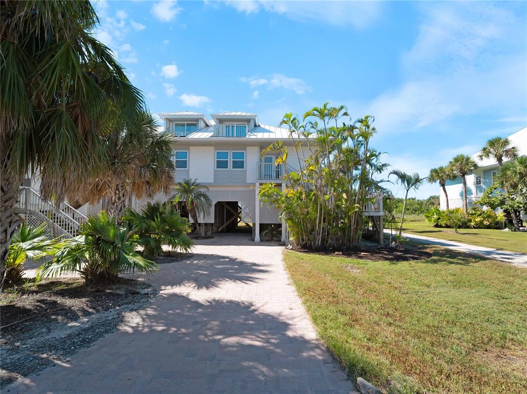 A two-story elevated house with a paved driveway and palm trees under a blue sky — 7104 PALM ISLAND DRIVE UNIT LE38, PLACIDA, FL
