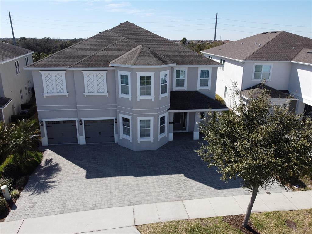 An aerial view shows a two-story suburban house with a paved driveway and gray exterior — 7666 FAIRFAX DRIVE, KISSIMMEE, FL