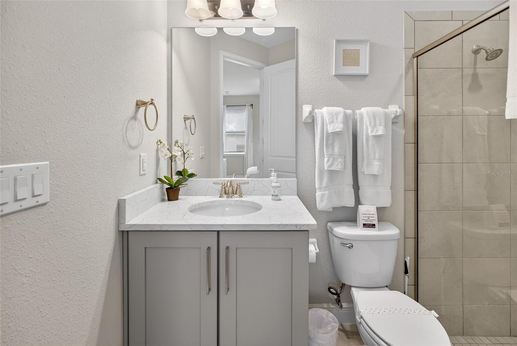 A bathroom features a gray vanity with a white countertop, a mirror, and a glass-enclosed shower — 7666 FAIRFAX DRIVE, KISSIMMEE, FL