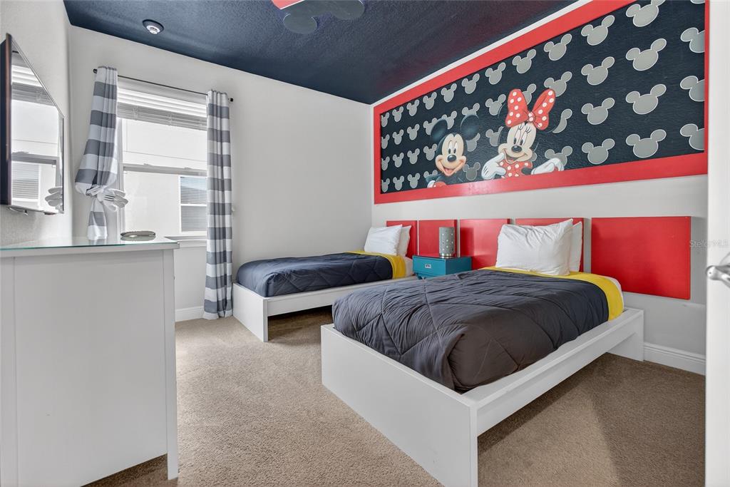 A bedroom features two twin beds, a Mickey Mouse themed wall mural, and carpeted flooring — 7666 FAIRFAX DRIVE, KISSIMMEE, FL