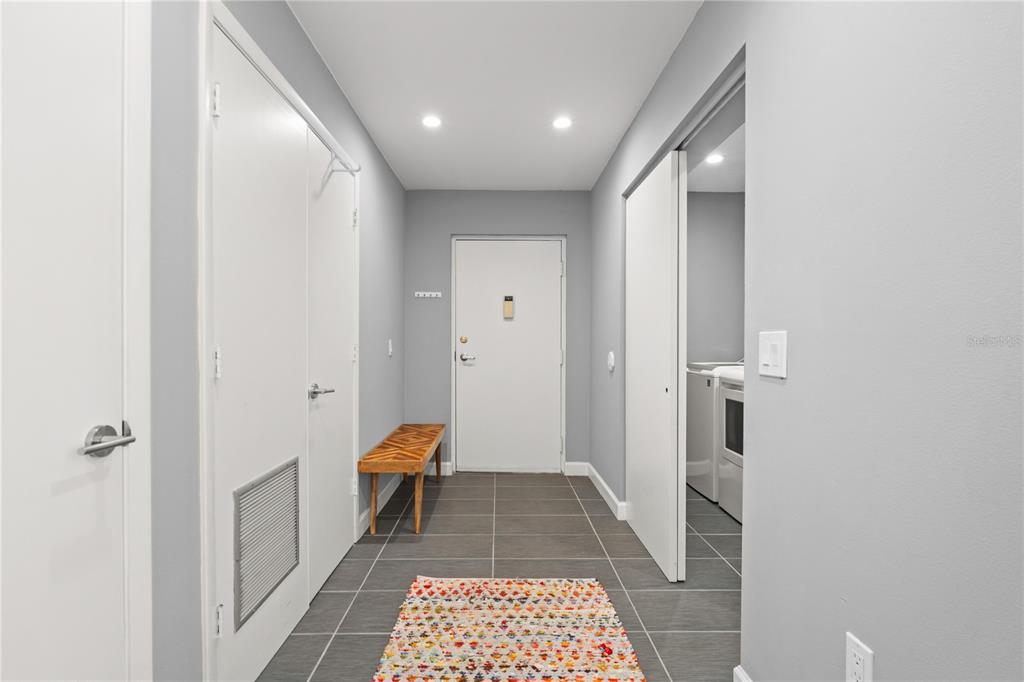 A hallway with gray tile flooring, a wooden bench, and a laundry closet with sliding doors — 2746 ORCHID OAKS DRIVE UNIT 301, SARASOTA, FL