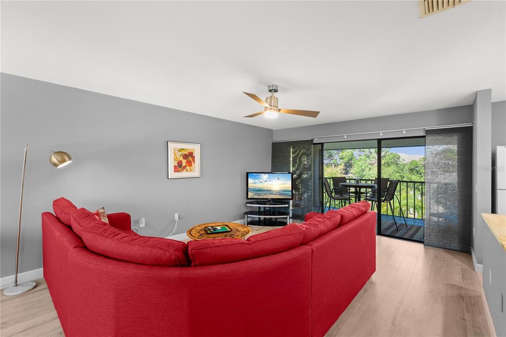 A living room features a red sectional sofa, a television, and a balcony with outdoor seating — 2746 ORCHID OAKS DRIVE UNIT 301, SARASOTA, FL