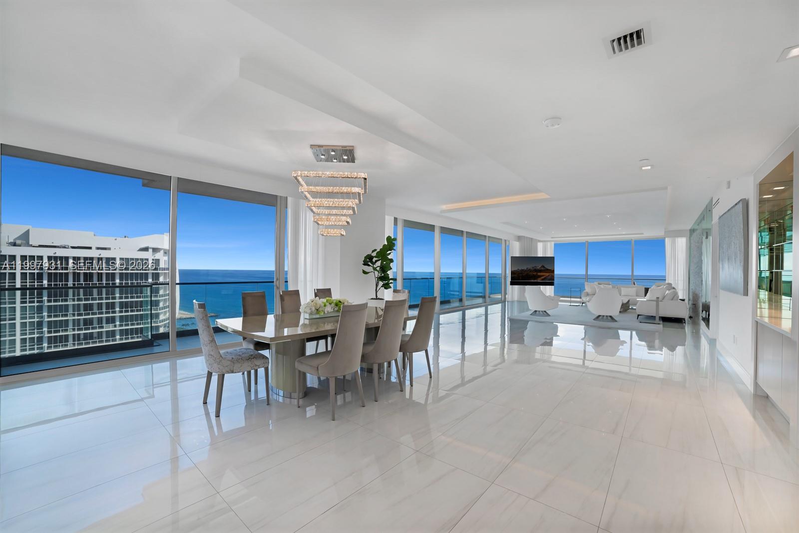 A modern dining and living area features floor-to-ceiling windows, white tile floors, and ocean views — 10203 Collins Ave # 2501, Bal Harbour FL 33154, BAL HARBOUR, FL