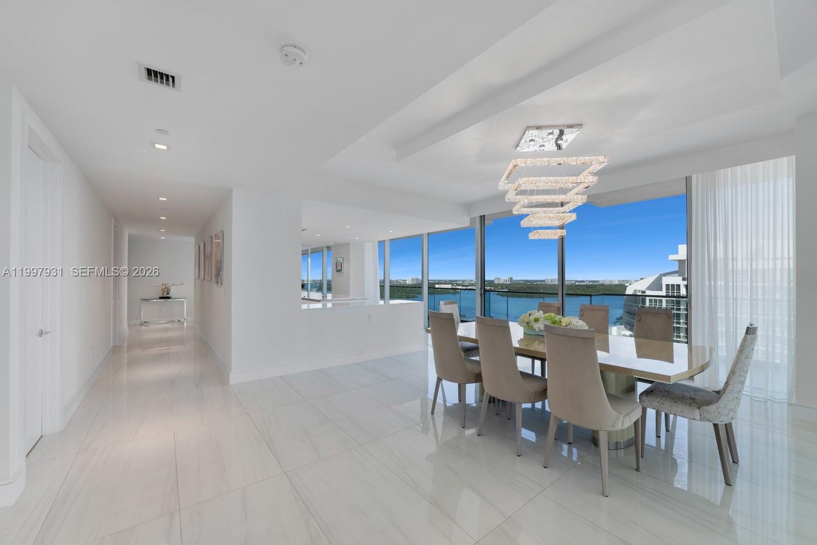 A dining room with a modern chandelier, marble floors, and floor-to-ceiling windows overlooking the water — 10203 Collins Ave # 2501, Bal Harbour FL 33154, BAL HARBOUR, FL