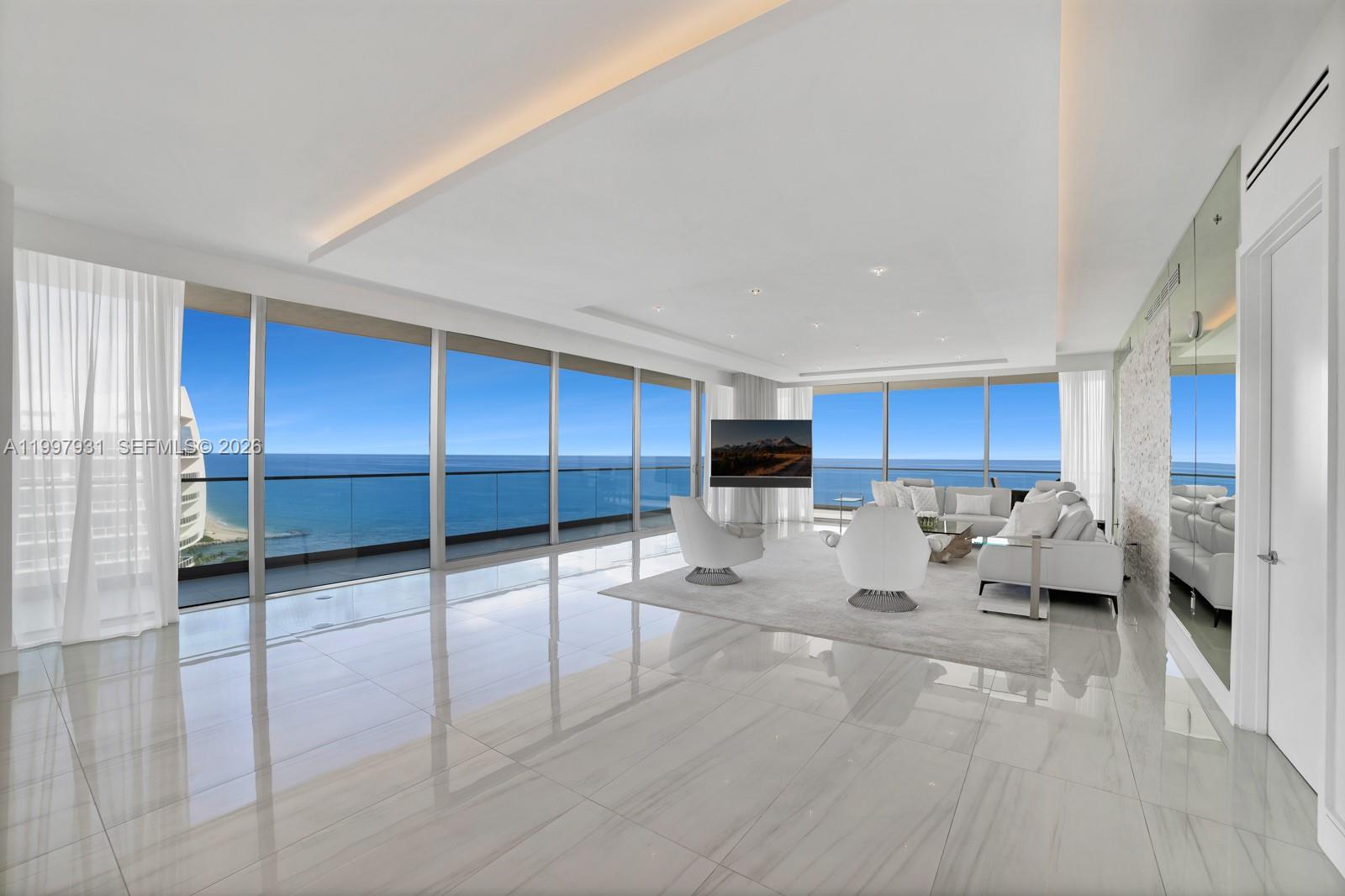 A modern living room features white tile floors, floor-to-ceiling windows, and panoramic ocean views — 10203 Collins Ave # 2501, Bal Harbour FL 33154, BAL HARBOUR, FL
