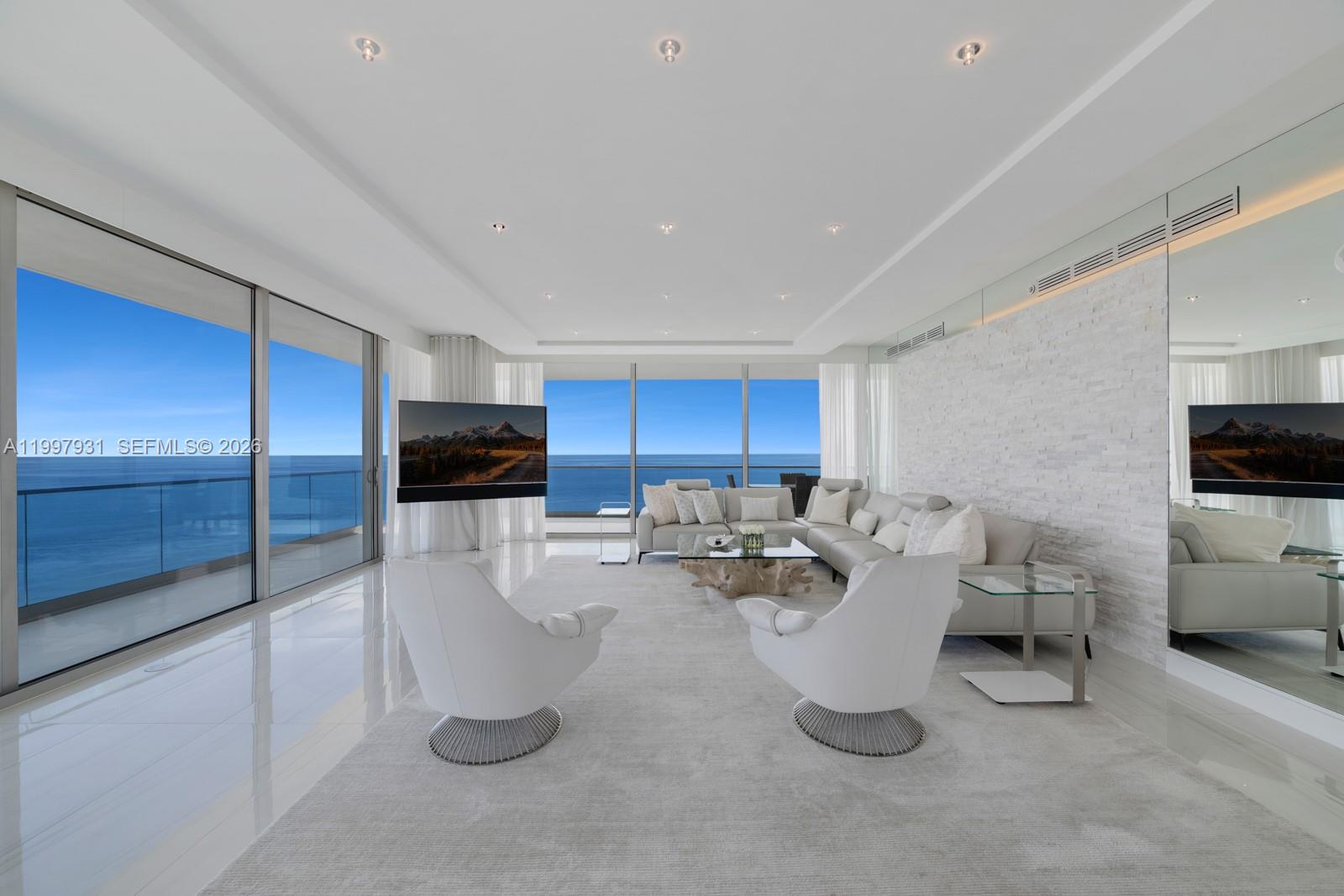 A modern living room features white tile floors, a stone accent wall, and ocean views — 10203 Collins Ave # 2501, Bal Harbour FL 33154, BAL HARBOUR, FL