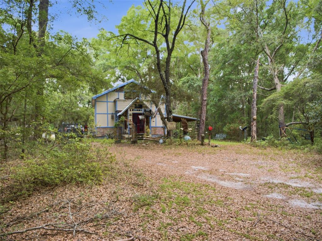 A two-story house with blue trim sits in a wooded area with a dirt driveway — 5229 SE 1ST STREET, TRENTON, FL