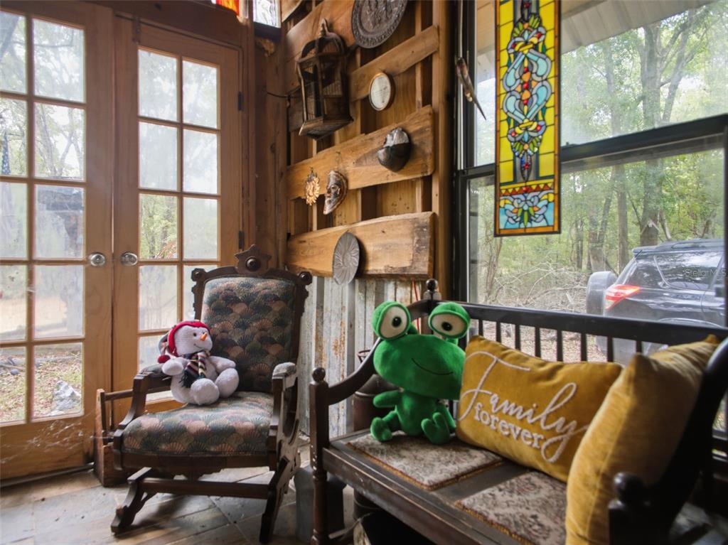 A rustic sunroom features wood-paneled walls, a rocking chair, a bench, and stained glass windows — 5229 SE 1ST STREET, TRENTON, FL