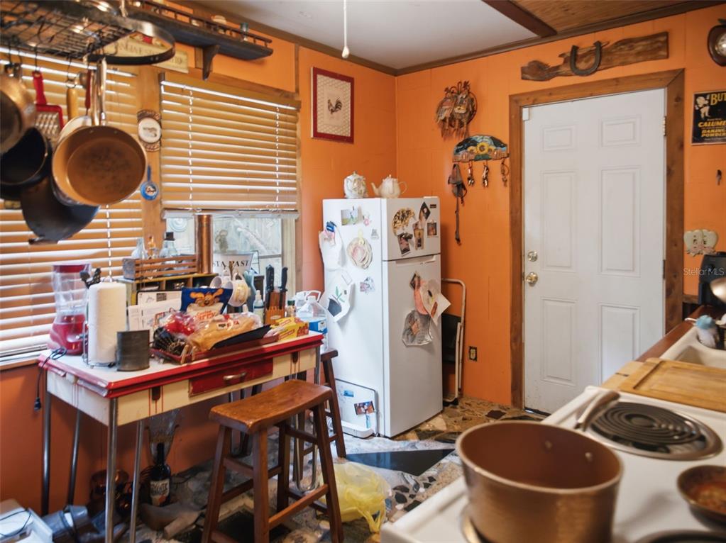 A kitchen with orange walls, a white refrigerator, a vintage-style table, and hanging cookware — 5229 SE 1ST STREET, TRENTON, FL
