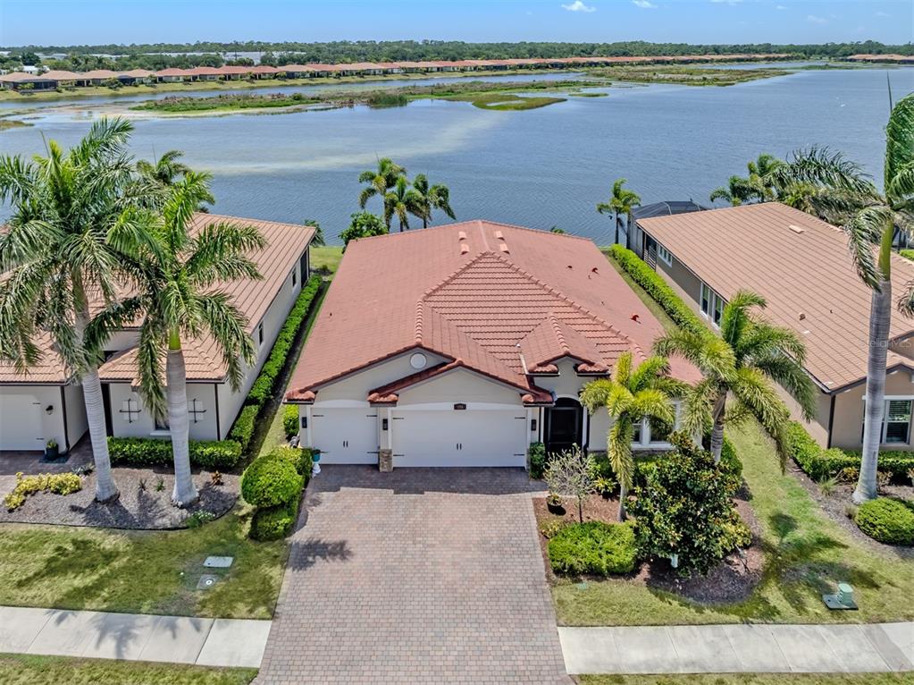 An aerial view of a suburban house with a tile roof, driveway, and waterfront backyard — 155 TOSCAVILLA BOULEVARD, NOKOMIS, FL