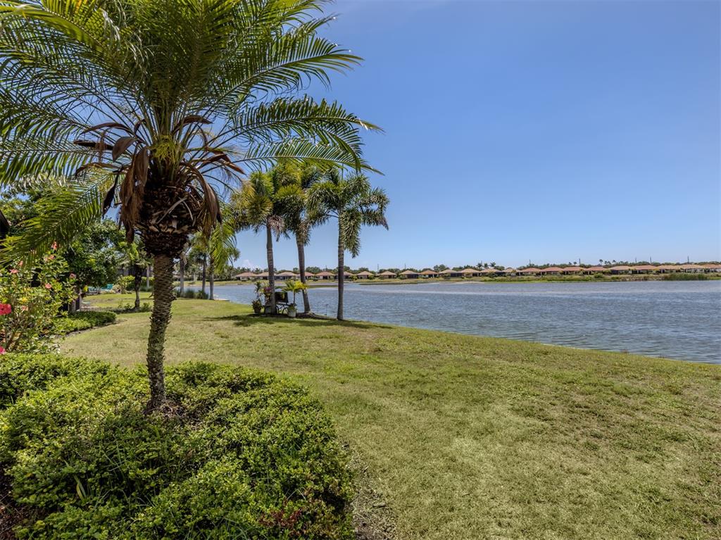 A grassy lawn with palm trees overlooks a lake with houses in the distance — 155 TOSCAVILLA BOULEVARD, NOKOMIS, FL