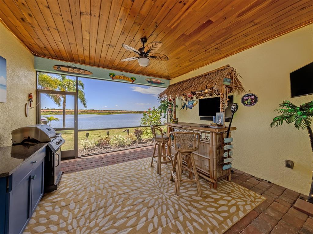 A covered patio features a tiki bar, outdoor grill, and a view of a lake — 155 TOSCAVILLA BOULEVARD, NOKOMIS, FL
