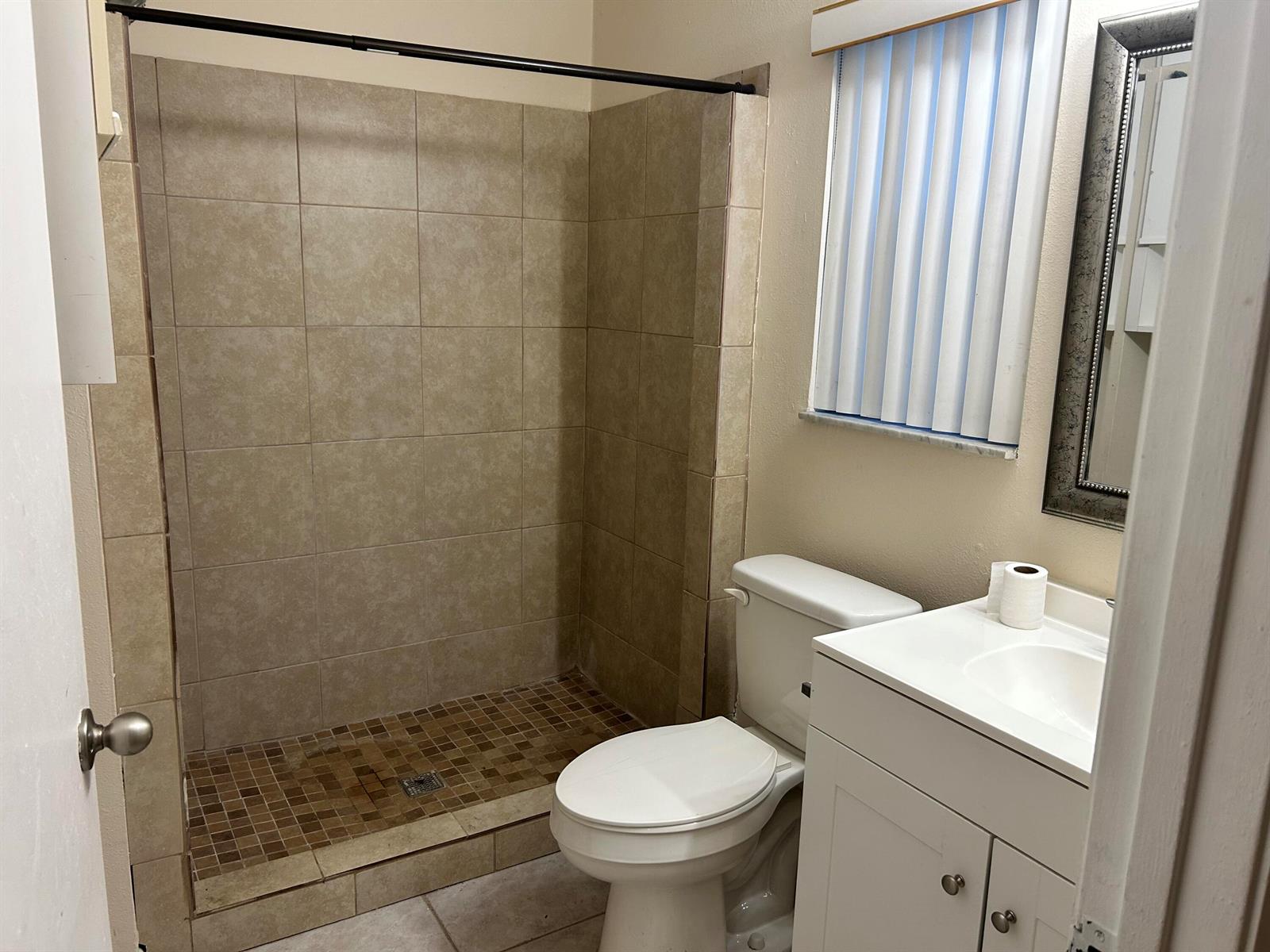 A bathroom features a tiled walk-in shower, a white toilet, and a vanity with a mirror — 23 Crossings Circle, Boynton Beach FL 33435, BOYNTON BEACH, FL