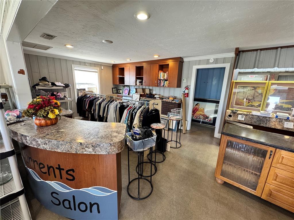 A salon interior features a curved reception desk, clothing racks, and wooden wall cabinets — 2924 KENILWORTH BOULEVARD, SEBRING, FL