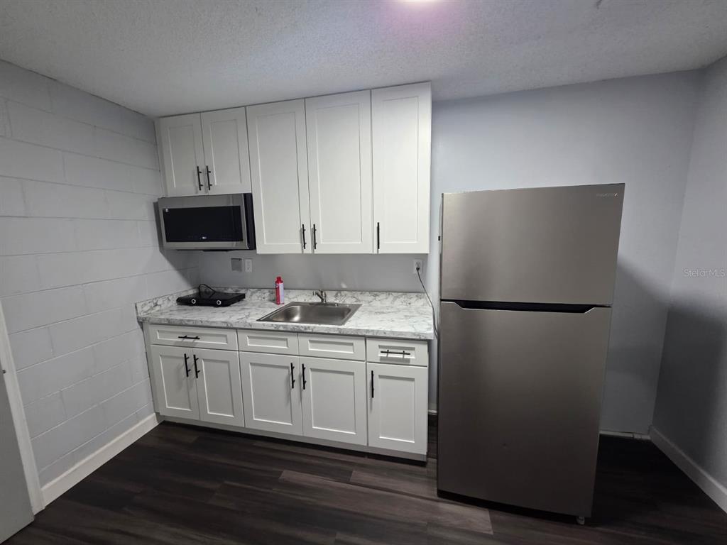A small kitchen features white cabinets, stainless steel appliances, and a marble-patterned countertop — 1326 SWEETWOOD BOULEVARD, KISSIMMEE, FL