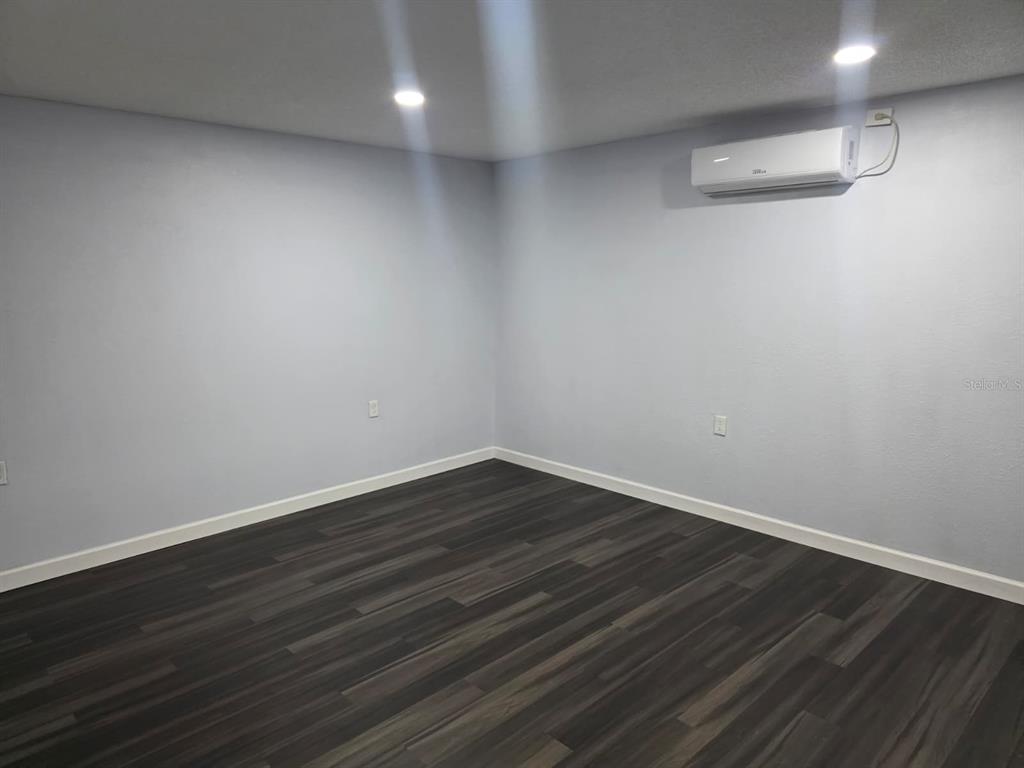 An empty room with light gray walls, dark wood-look flooring, and a wall-mounted air conditioner — 1326 SWEETWOOD BOULEVARD, KISSIMMEE, FL