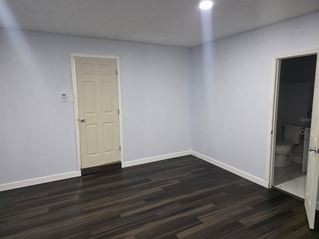 A room with light blue walls, dark wood-look flooring, a closed door, and an open bathroom — 1326 SWEETWOOD BOULEVARD, KISSIMMEE, FL
