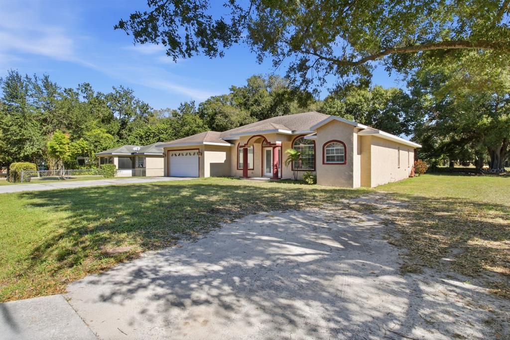 A single-story house with a tan stucco exterior, red trim, and a concrete driveway — 1218 37TH STREET NW, WINTER HAVEN, FL