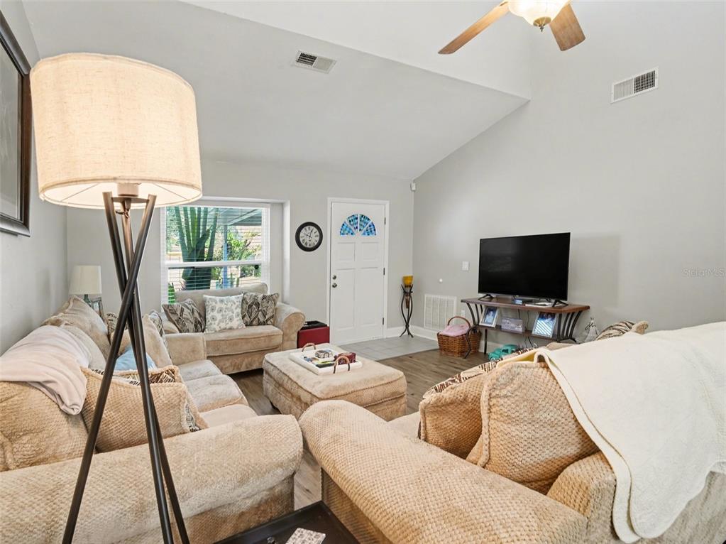 A living room features beige furniture, a television on a stand, and a vaulted ceiling — 5627 35TH COURT E, BRADENTON, FL