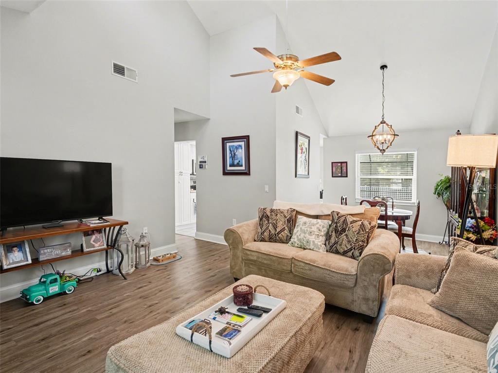 A living room with vaulted ceilings, wood-look flooring, a ceiling fan, and a dining area — 5627 35TH COURT E, BRADENTON, FL