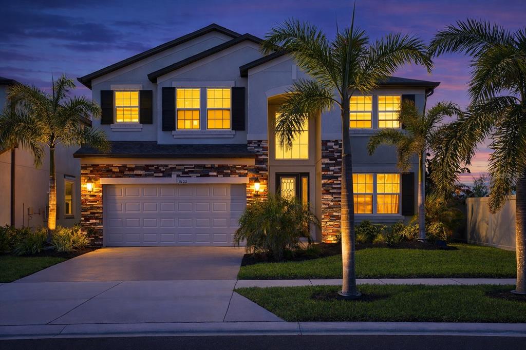 A two-story suburban house with a stone facade, two-car garage, and palm trees at dusk — 3103 MARINE GRASS DRIVE, WIMAUMA, FL