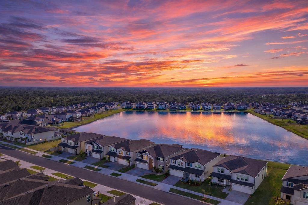 An aerial view of a suburban neighborhood featuring houses surrounding a central retention pond at sunset — 3103 MARINE GRASS DRIVE, WIMAUMA, FL