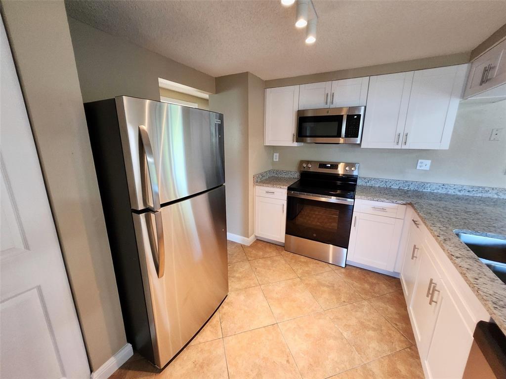 A kitchen with white cabinets, granite countertops, stainless steel appliances, and light-colored tile flooring — 7146 CARMEL AVENUE, NEW PORT RICHEY, FL