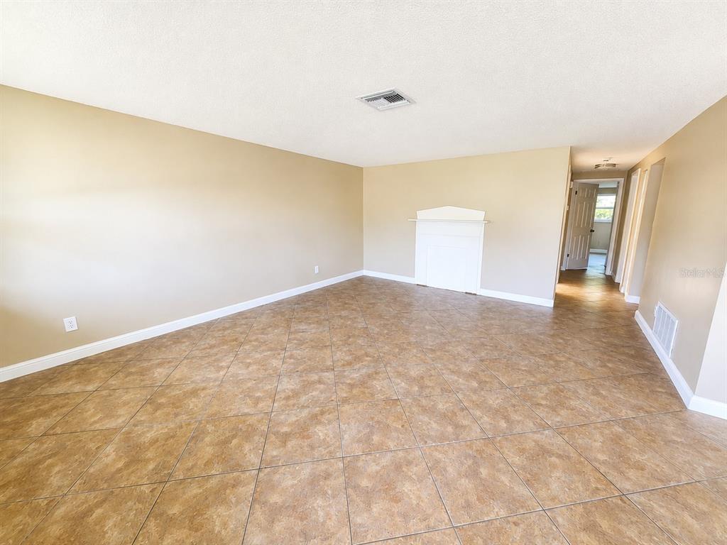 An empty room with tan walls, a white fireplace mantel, and diagonal brown tile flooring — 7146 CARMEL AVENUE, NEW PORT RICHEY, FL