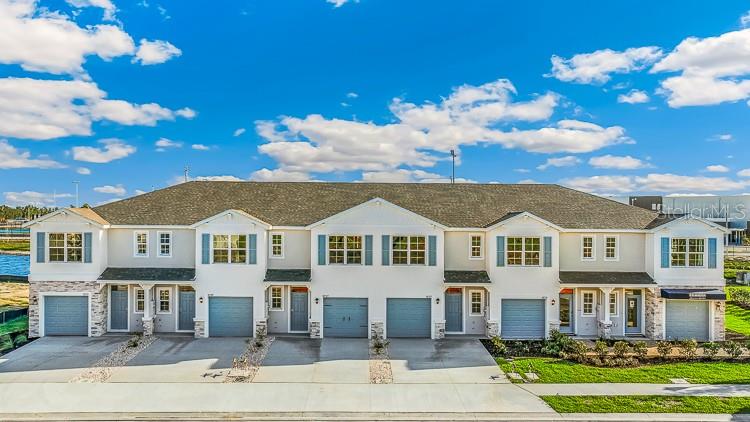 A multi-unit residential building with light-colored siding, stone accents, and multiple garage doors — 10707 TIGER LILY DRIVE, VENICE, FL