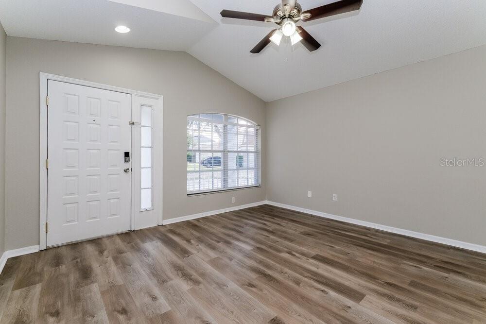 An empty room with light gray walls, wood-look flooring, a ceiling fan, and a front door — 6123 SAND KEY LANE, WESLEY CHAPEL, FL