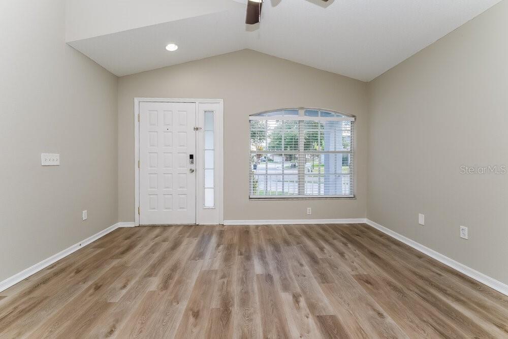 An empty room with light wood-look flooring, a vaulted ceiling, and a front entryway — 6123 SAND KEY LANE, WESLEY CHAPEL, FL