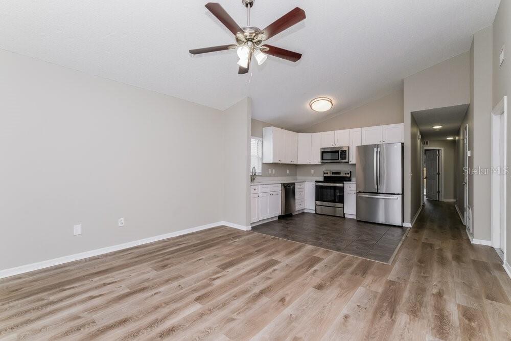 An open-concept kitchen with white cabinets and stainless steel appliances overlooks a wood-floored living area — 6123 SAND KEY LANE, WESLEY CHAPEL, FL