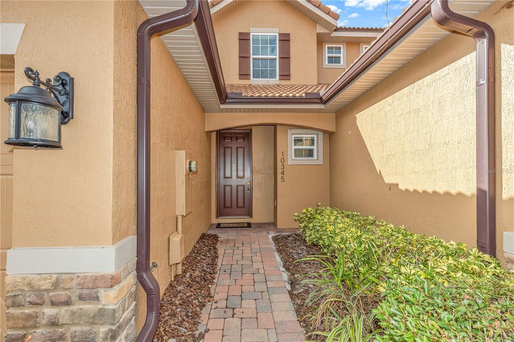 A paved walkway leads to the front entrance of a house with tan stucco walls — 10345 BELFRY CIRCLE, ORLANDO, FL