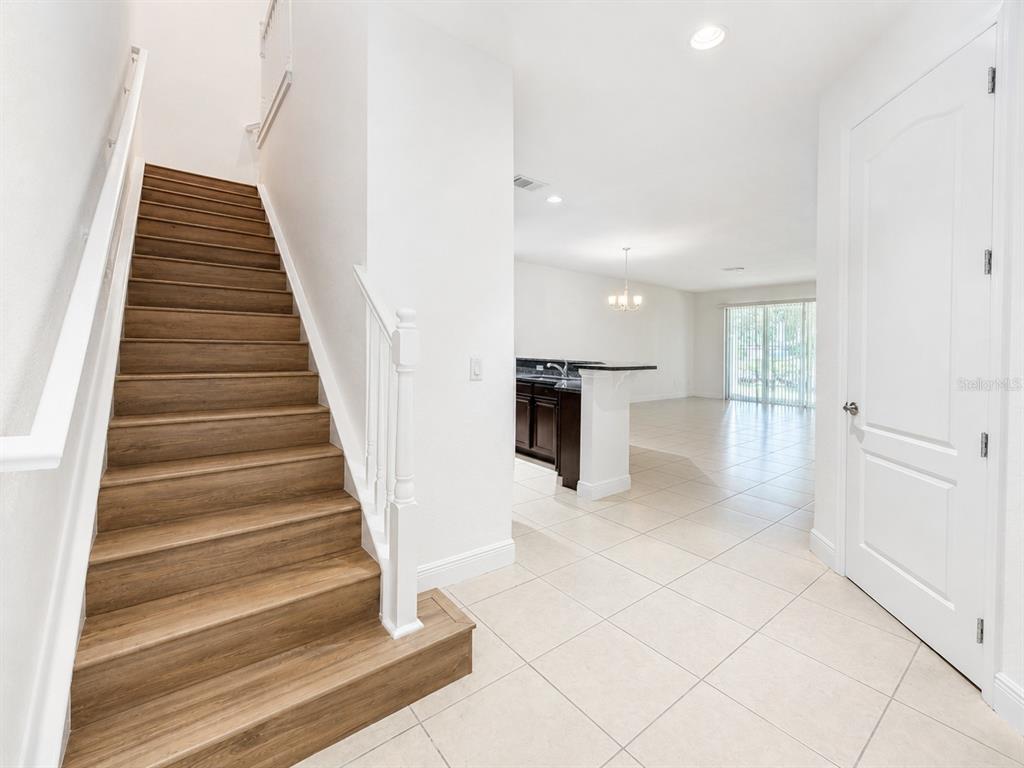 A staircase with wood-look steps leads upward next to a tiled entryway and kitchen area — 10345 BELFRY CIRCLE, ORLANDO, FL