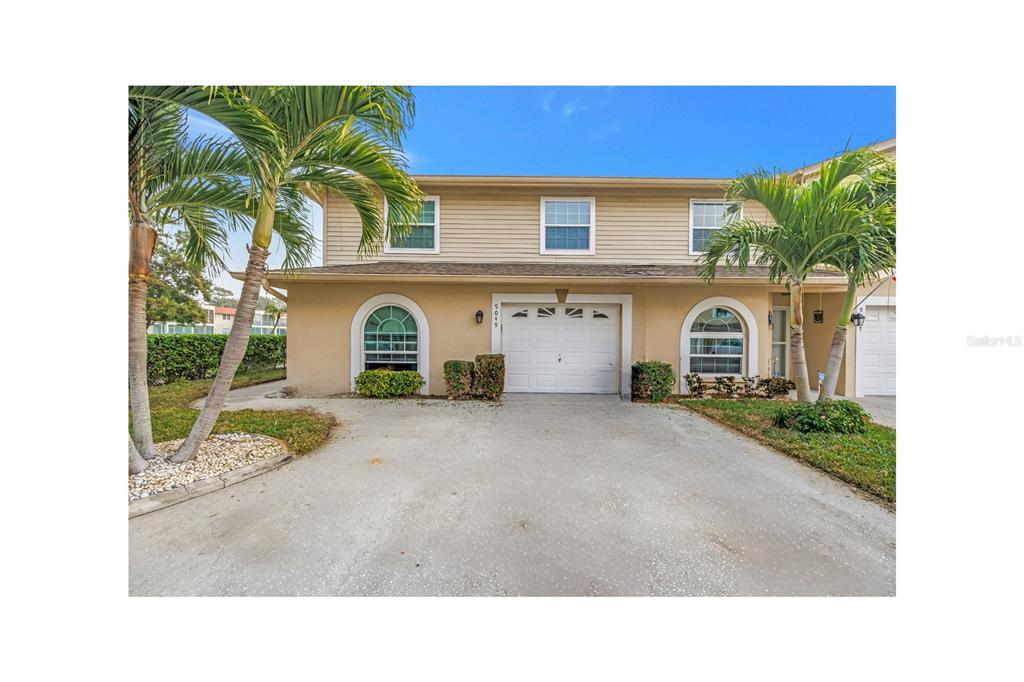 A two-story townhouse with a beige exterior, arched windows, and a single-car garage — 9049 ANTIGUA DRIVE, SEMINOLE, FL