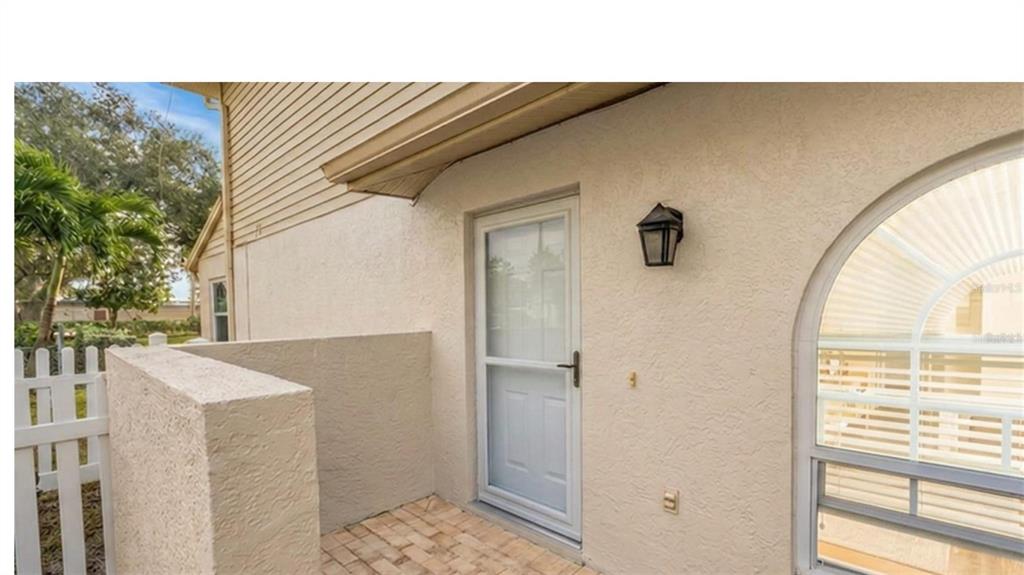 A paved patio area features a white storm door, exterior wall sconce, and stucco siding — 9049 ANTIGUA DRIVE, SEMINOLE, FL