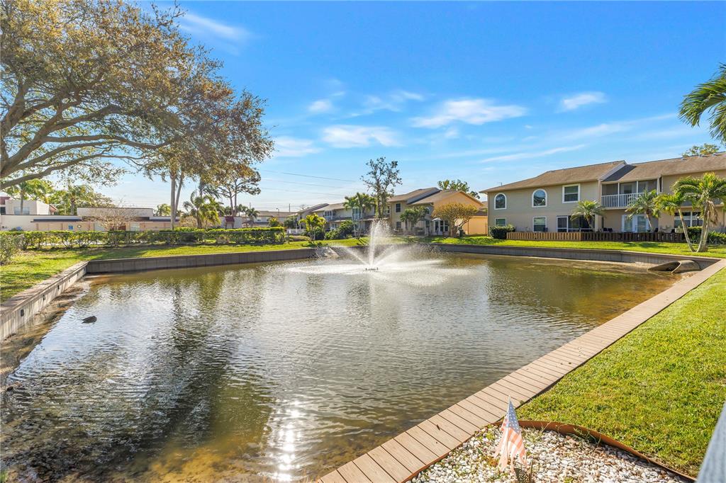 A pond with a central fountain sits in front of multi-story residential buildings — 9049 ANTIGUA DRIVE, SEMINOLE, FL