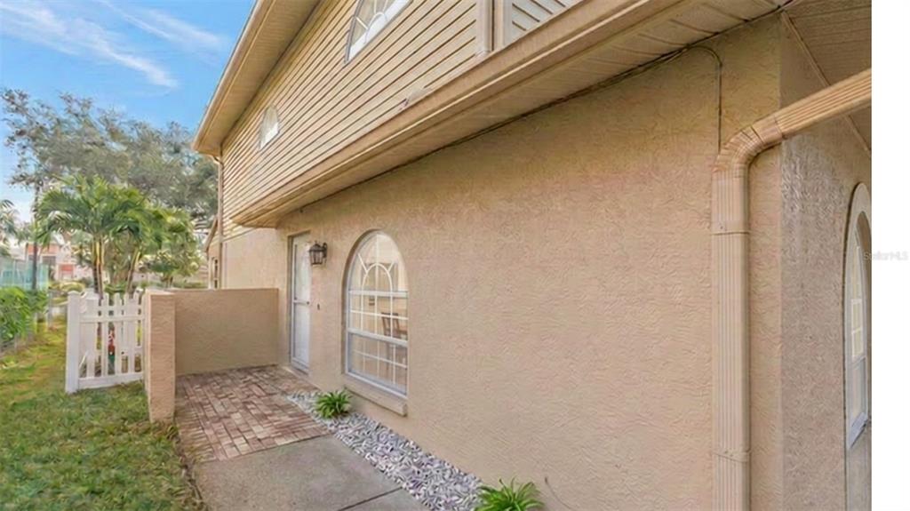A beige stucco exterior wall features an arched window, a side door, and a brick patio — 9049 ANTIGUA DRIVE, SEMINOLE, FL