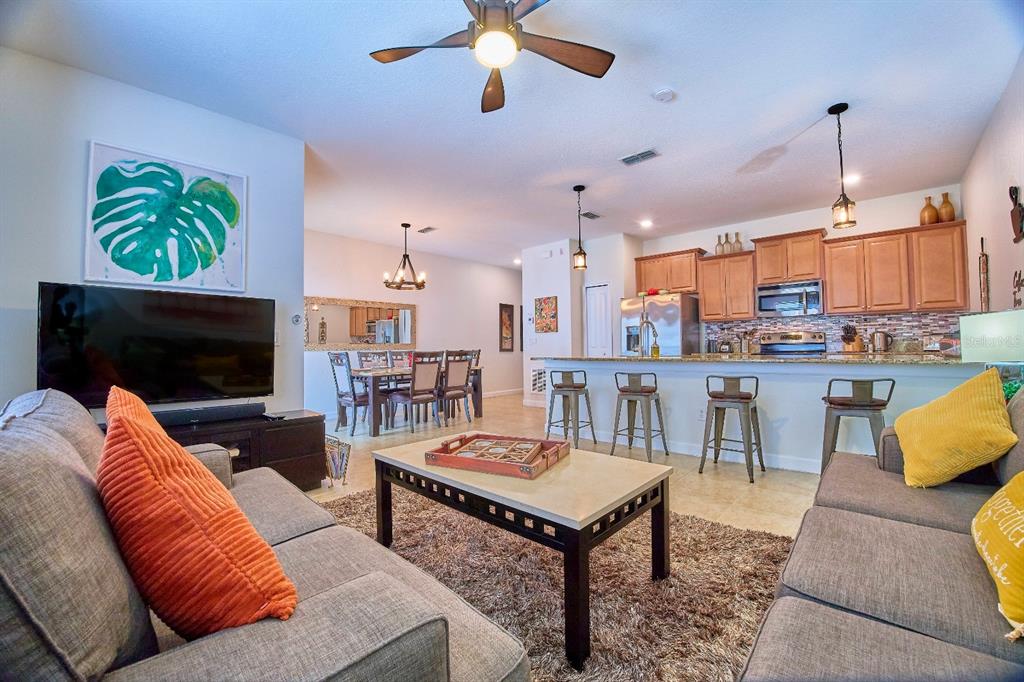 A living room with a gray sofa and coffee table opens to a kitchen with barstools — 4821 BRIER ROSE LANE, KISSIMMEE, FL