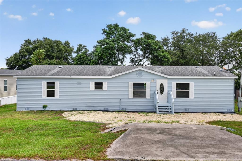 A light blue single-story manufactured home features a concrete driveway and a small front porch — 225 SKYLINE DRIVE, LADY LAKE, FL