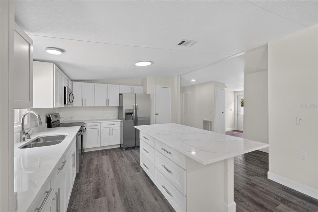 A modern kitchen features white cabinets, a large marble-topped island, and stainless steel appliances — 225 SKYLINE DRIVE, LADY LAKE, FL