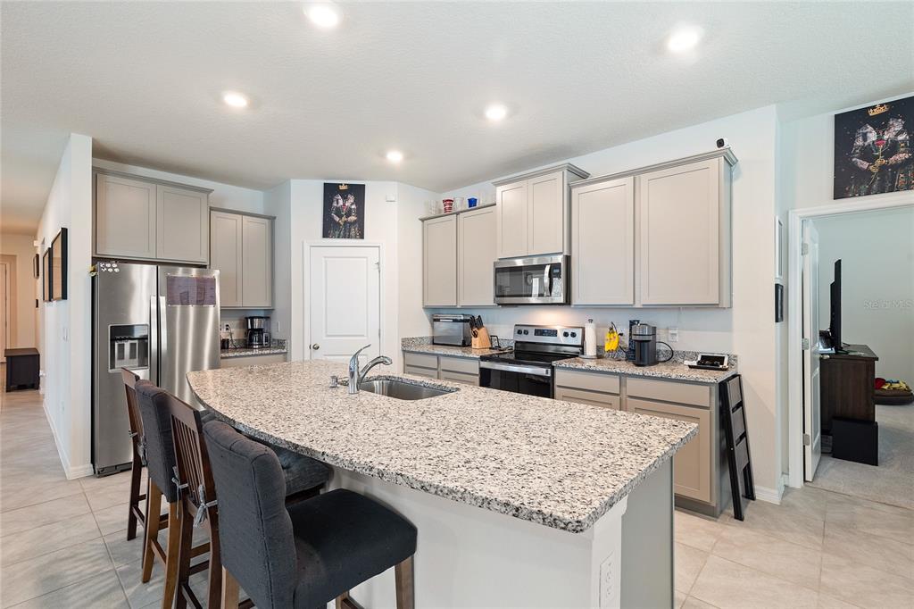 A kitchen features gray cabinets, granite countertops, a large island, and stainless steel appliances — 12401 SHINING WILLOW STREET, RIVERVIEW, FL