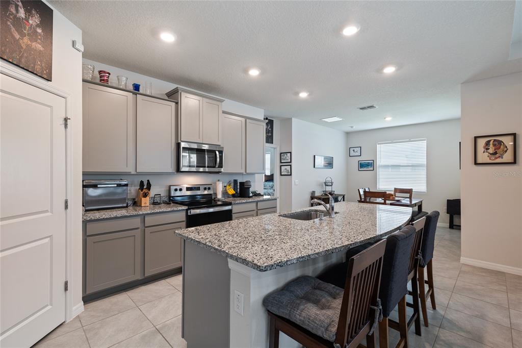 A kitchen features gray cabinetry, granite countertops, a center island with seating, and tile flooring — 12401 SHINING WILLOW STREET, RIVERVIEW, FL