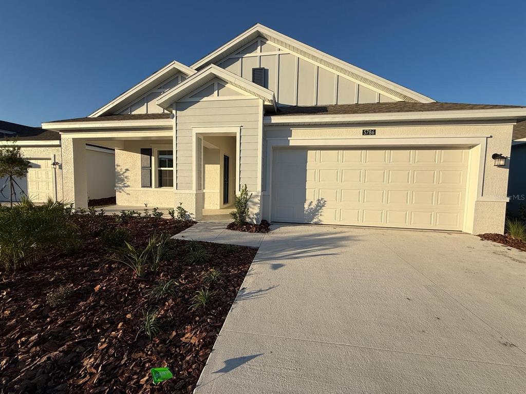 A light-colored single-story house features a two-car garage, a covered entryway, and landscaped mulch beds — 5786 GINGHAM DRIVE, KISSIMMEE, FL