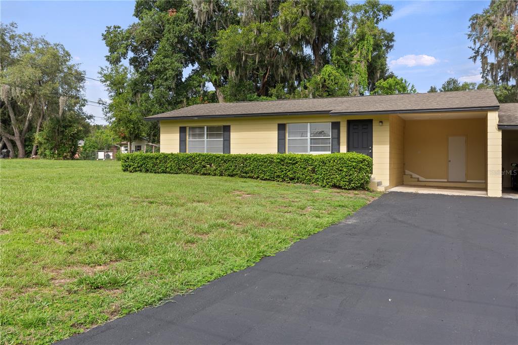 A single-story yellow house with a black driveway and a covered carport — 12215 LEANNE DRIVE, DADE CITY, FL
